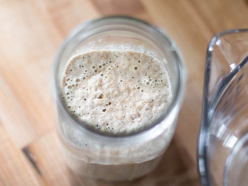 Bubbly sourdough starter in a glass jar, seen from above on a wooden counter